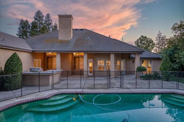 pool at dusk featuring a patio and an outdoor kitchen