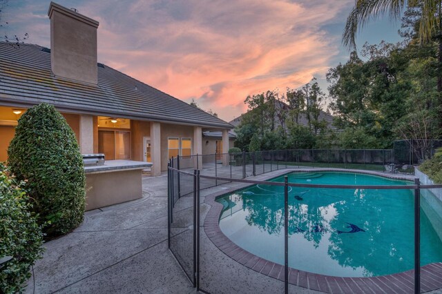 pool at dusk with an outdoor kitchen and a patio