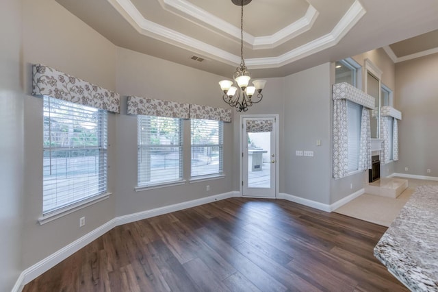 interior space featuring an inviting chandelier, ornamental molding, a tray ceiling, dark hardwood / wood-style flooring, and a fireplace