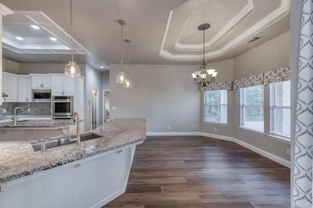 kitchen featuring light stone countertops, pendant lighting, white cabinets, and a tray ceiling