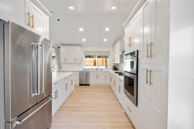 kitchen with tasteful backsplash, white cabinetry, sink, stainless steel appliances, and light hardwood / wood-style flooring