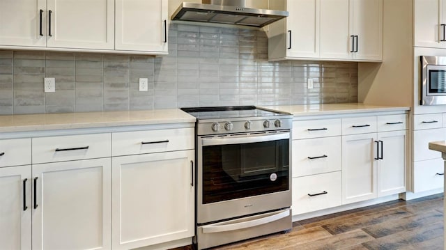 kitchen with wall chimney range hood, dark wood-type flooring, backsplash, stainless steel appliances, and white cabinets