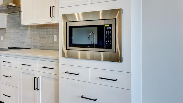 kitchen featuring stainless steel microwave, tasteful backsplash, white cabinetry, light stone counters, and wall chimney exhaust hood