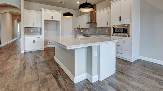 kitchen with stainless steel microwave, an island with sink, hanging light fixtures, and white cabinets