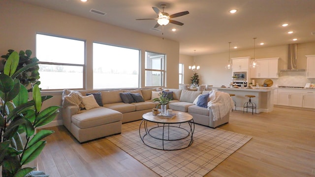 living room with plenty of natural light, ceiling fan with notable chandelier, and light wood-type flooring