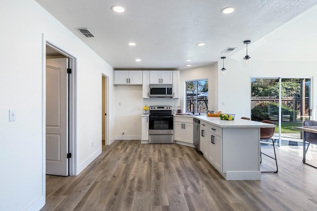 kitchen with white cabinetry, stainless steel appliances, kitchen peninsula, hanging light fixtures, and a breakfast bar area