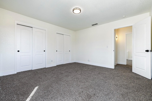 unfurnished bedroom featuring dark colored carpet, a textured ceiling, and two closets