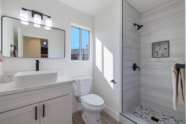 bathroom featuring toilet, wood-type flooring, vanity, and a tile shower