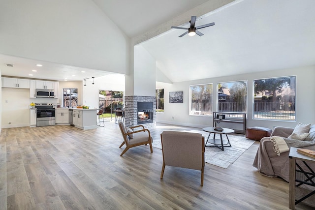 living room featuring high vaulted ceiling, light hardwood / wood-style floors, ceiling fan, a fireplace, and beamed ceiling