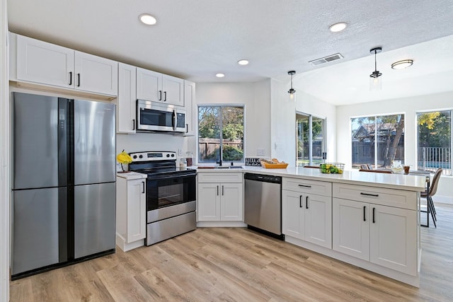 kitchen with white cabinets, hanging light fixtures, stainless steel appliances, and light hardwood / wood-style floors