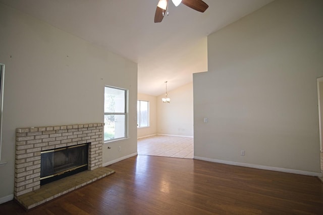 unfurnished living room featuring hardwood / wood-style flooring, lofted ceiling, ceiling fan with notable chandelier, and a brick fireplace