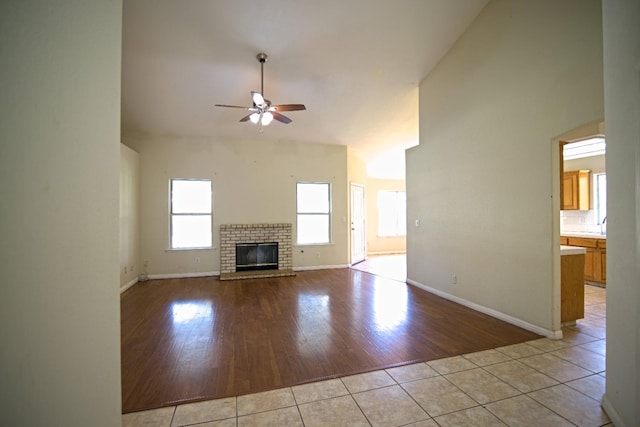 unfurnished living room with ceiling fan, a towering ceiling, a fireplace, and light tile patterned floors