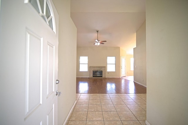 unfurnished living room with high vaulted ceiling, light tile patterned floors, a fireplace, and ceiling fan