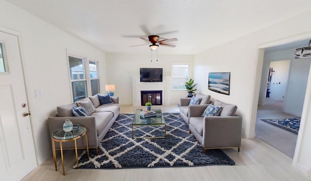 living room with a wealth of natural light, a glass covered fireplace, a ceiling fan, and wood finished floors