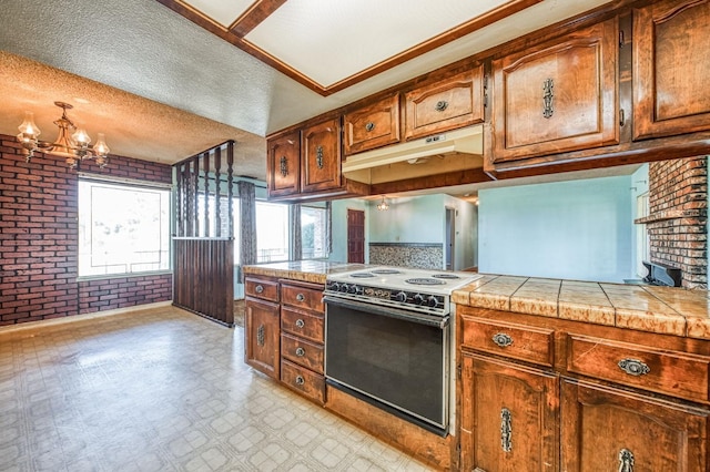 kitchen featuring an inviting chandelier, a textured ceiling, tile counters, range with electric cooktop, and brick wall