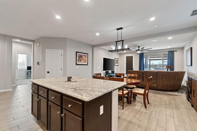 kitchen featuring pendant lighting, a center island, light stone counters, dark brown cabinetry, and light wood-type flooring