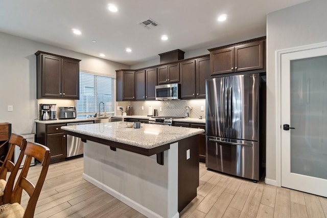 kitchen with stainless steel appliances, light stone countertops, a center island, and light wood-type flooring