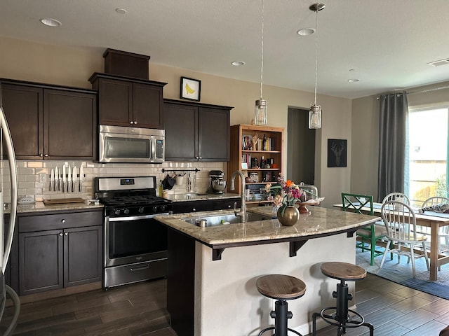 kitchen featuring sink, light stone counters, an island with sink, pendant lighting, and stainless steel appliances