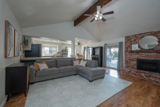 living room featuring hardwood / wood-style floors, high vaulted ceiling, a fireplace, beamed ceiling, and ceiling fan