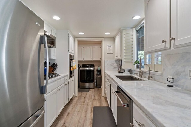 kitchen featuring appliances with stainless steel finishes, separate washer and dryer, sink, white cabinets, and light hardwood / wood-style floors