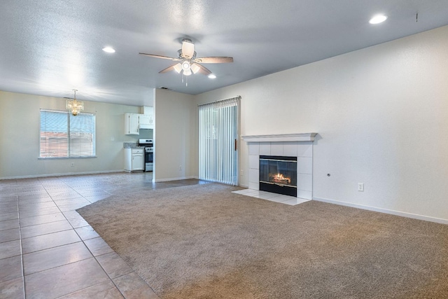 unfurnished living room with light colored carpet, ceiling fan with notable chandelier, a tile fireplace, and a textured ceiling