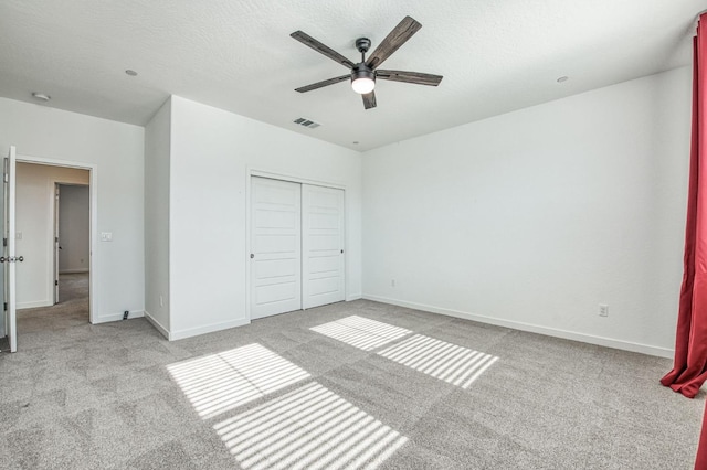 unfurnished bedroom with light carpet, ceiling fan, a closet, and a textured ceiling