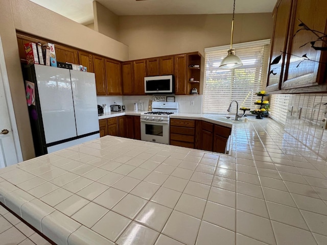 kitchen featuring vaulted ceiling, tile countertops, decorative light fixtures, sink, and white appliances