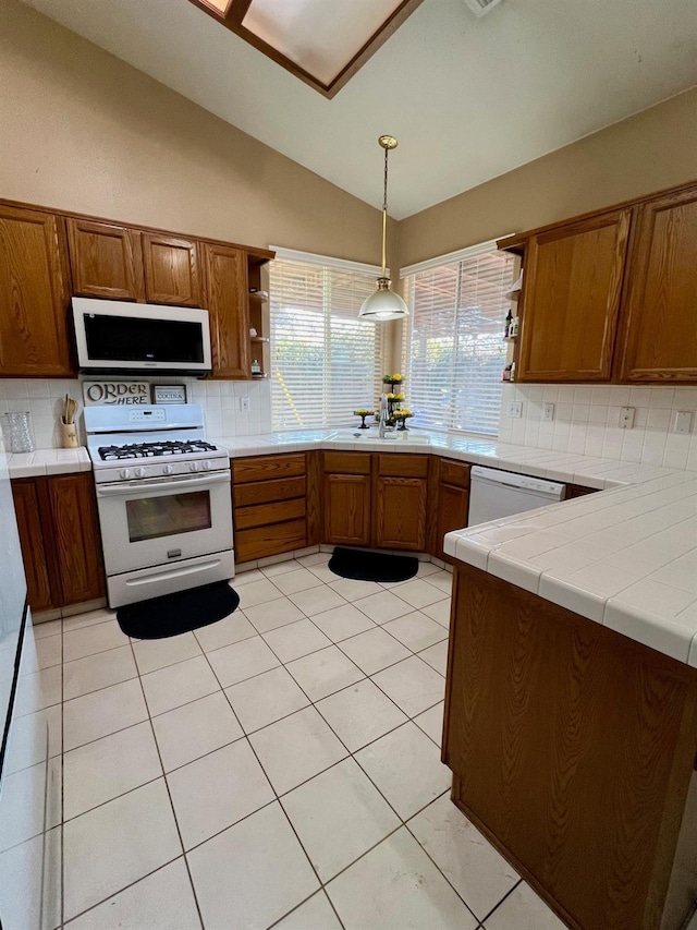 kitchen featuring tile countertops, lofted ceiling, hanging light fixtures, light tile patterned floors, and white appliances