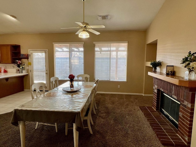 carpeted dining space with a brick fireplace and ceiling fan