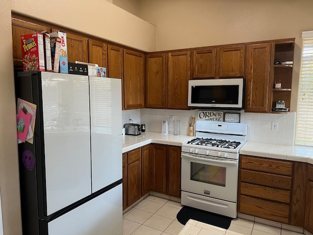 kitchen with backsplash, white appliances, tile counters, and light tile patterned floors