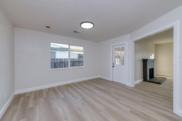 interior space featuring a brick fireplace, a healthy amount of sunlight, a textured ceiling, and light hardwood / wood-style floors