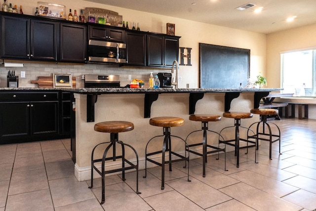 kitchen with stainless steel appliances, a breakfast bar, a center island with sink, and backsplash