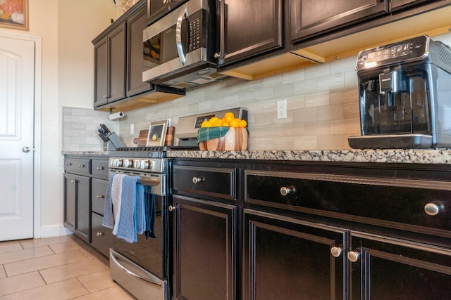 kitchen with light tile patterned flooring, appliances with stainless steel finishes, tasteful backsplash, light stone counters, and dark brown cabinets