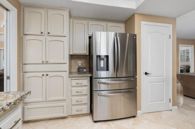 kitchen with tasteful backsplash, cream cabinets, light stone countertops, and stainless steel fridge with ice dispenser