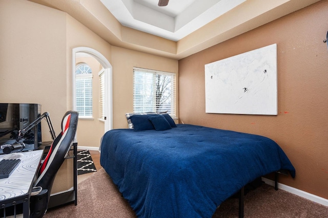 bedroom with ceiling fan, a tray ceiling, and dark colored carpet