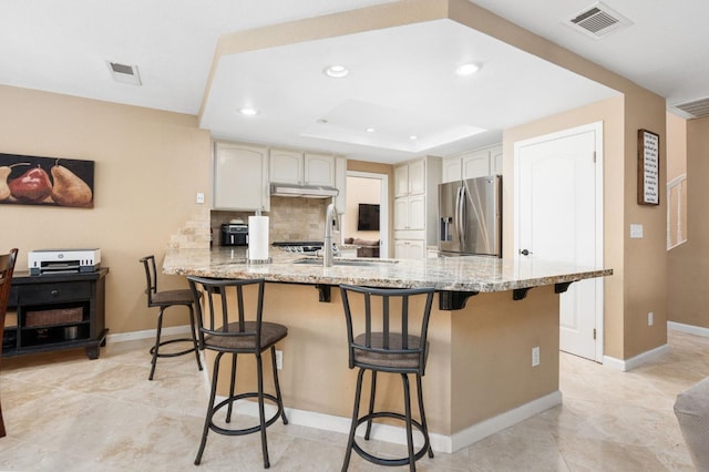 kitchen featuring light stone counters, stainless steel fridge with ice dispenser, kitchen peninsula, and a breakfast bar