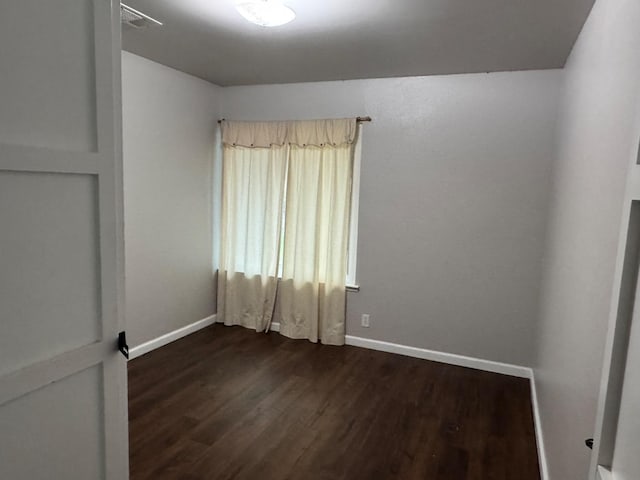 empty room with dark wood-style flooring, visible vents, and baseboards