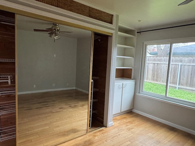 spare room with built in shelves, light wood finished floors, a ceiling fan, and baseboards