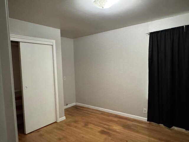 unfurnished bedroom with a closet, wood finished floors, and baseboards