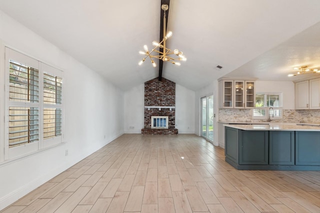 kitchen with white cabinetry, a brick fireplace, hanging light fixtures, a notable chandelier, and backsplash