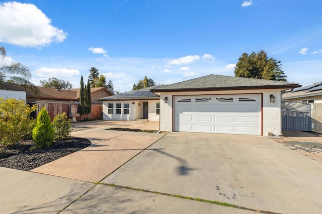 ranch-style home with a garage, fence, driveway, roof mounted solar panels, and stucco siding