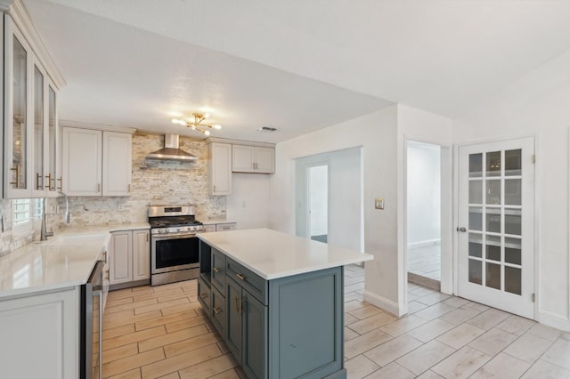 kitchen with a center island, stainless steel appliances, light countertops, glass insert cabinets, and wall chimney range hood