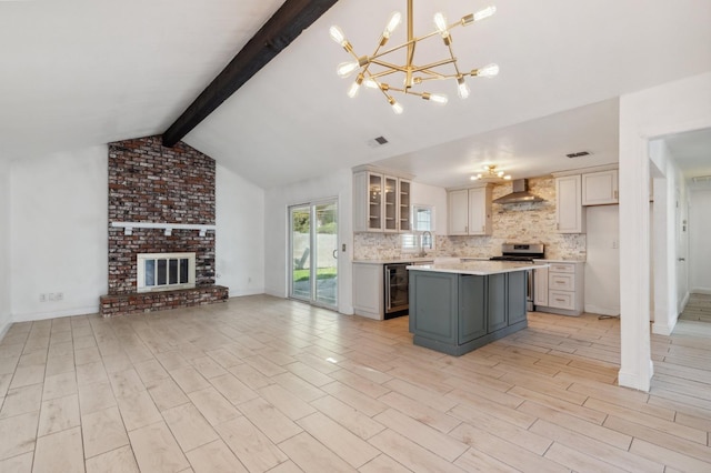 kitchen featuring stainless steel stove, open floor plan, light countertops, hanging light fixtures, and wall chimney exhaust hood