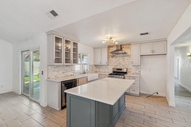 kitchen featuring glass insert cabinets, a center island, light countertops, wall chimney range hood, and gas stove