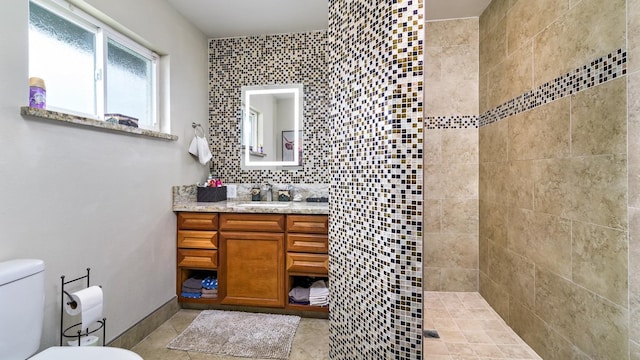 bathroom featuring a tile shower, backsplash, tile patterned flooring, vanity, and toilet