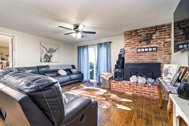 living room featuring dark wood-type flooring, ceiling fan, a brick fireplace, and a textured ceiling