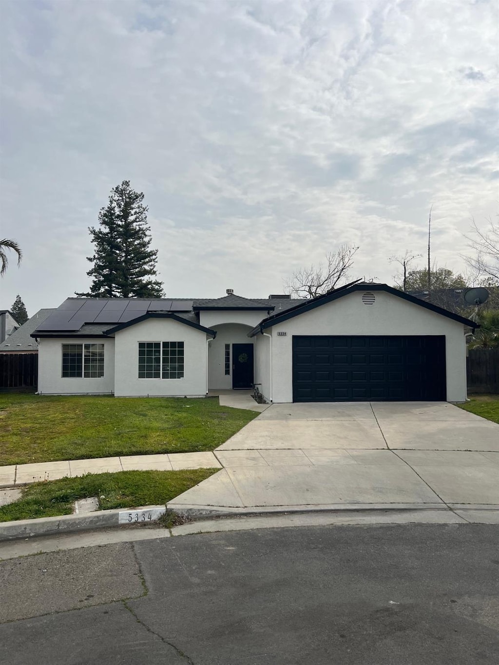 single story home featuring a garage, a front yard, and solar panels