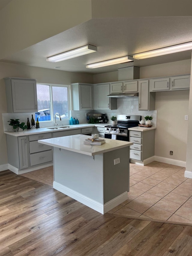 kitchen with sink, stainless steel range with electric cooktop, decorative backsplash, a center island, and light wood-type flooring