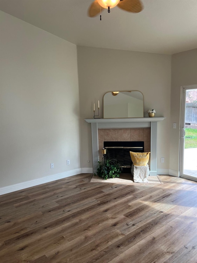 unfurnished living room featuring a tiled fireplace, hardwood / wood-style floors, and ceiling fan