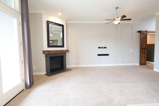 unfurnished living room featuring a fireplace, light colored carpet, a barn door, and ceiling fan